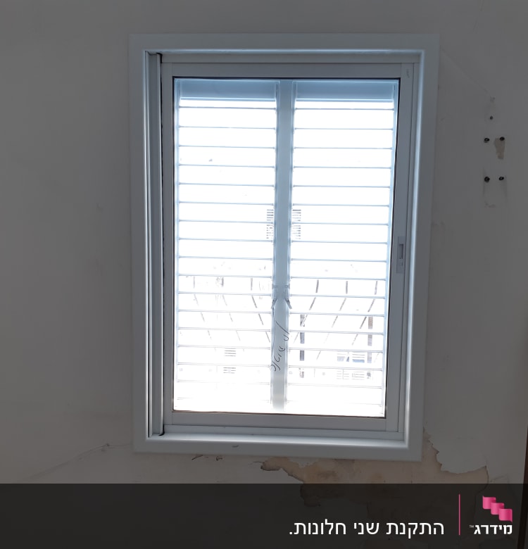 חלון אלומיניום עם תריסים סגורים על קיר לבן